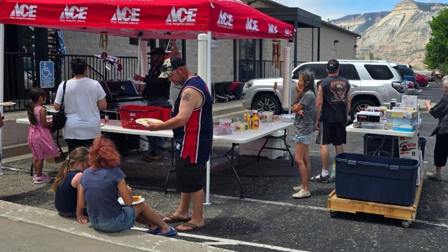 Customers gather around grills and refreshment tables during an outdoor Ace Hardware parking lot event.